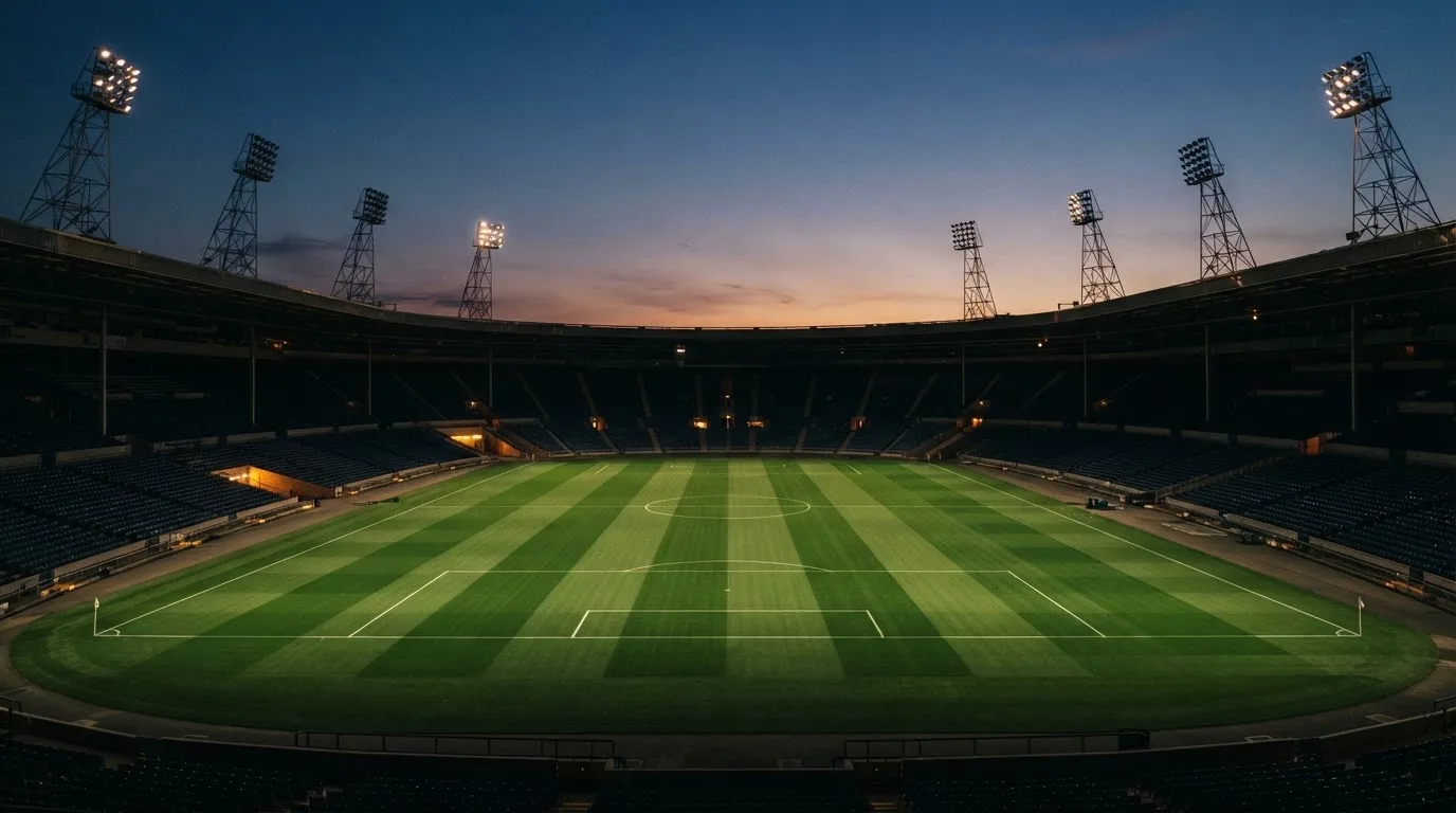 Een leeg voetbalstadion met lichtmasten bij schemering