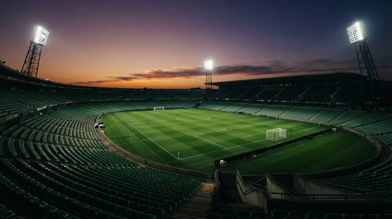 Een leeg voetbalstadion met lichtmasten bij schemering
