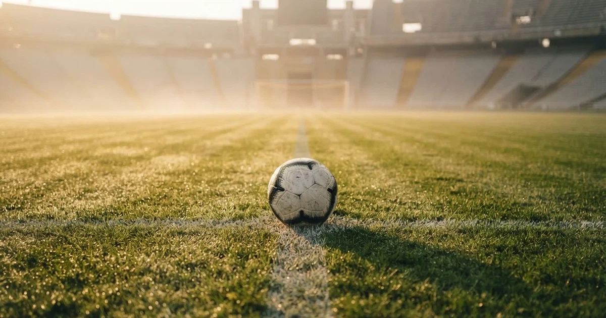 Een voetbal op de middenstip van een grasveld in het ochtendlicht
