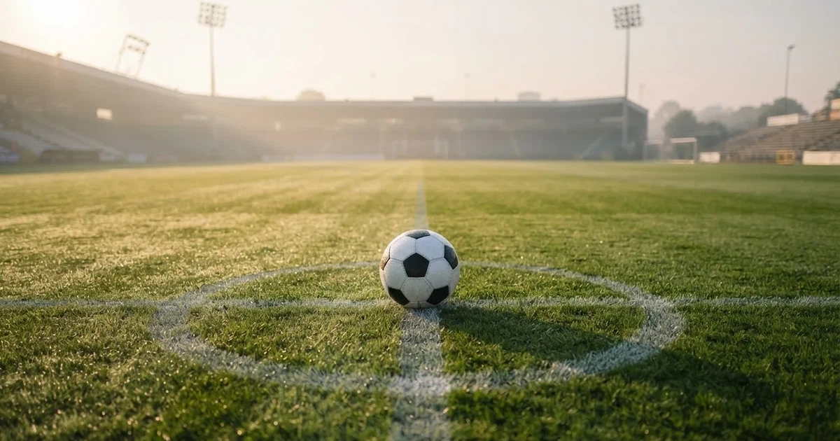 Een voetbal op de middenstip van een grasveld in het ochtendlicht