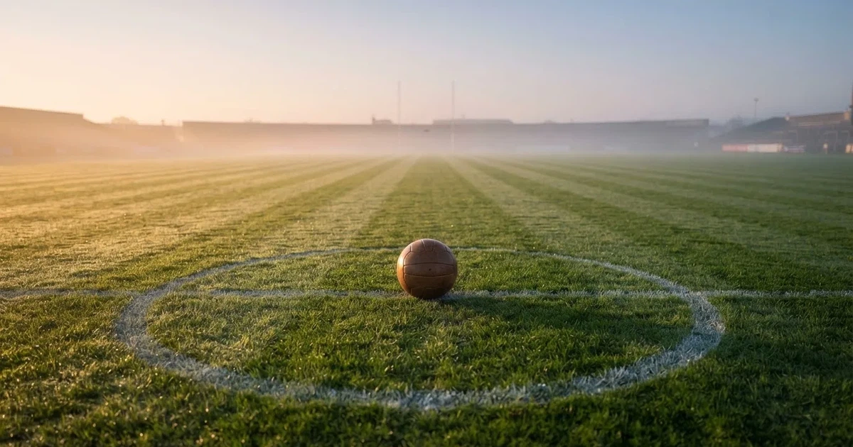 Een voetbal op de middenstip van een grasveld in het ochtendlicht