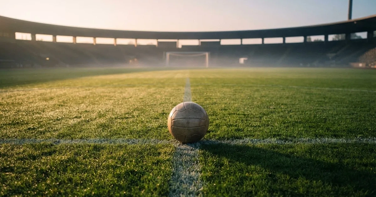 Een voetbal op de middenstip van een grasveld in het ochtendlicht