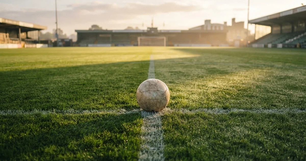 Een voetbal op de middenstip van een grasveld in het ochtendlicht