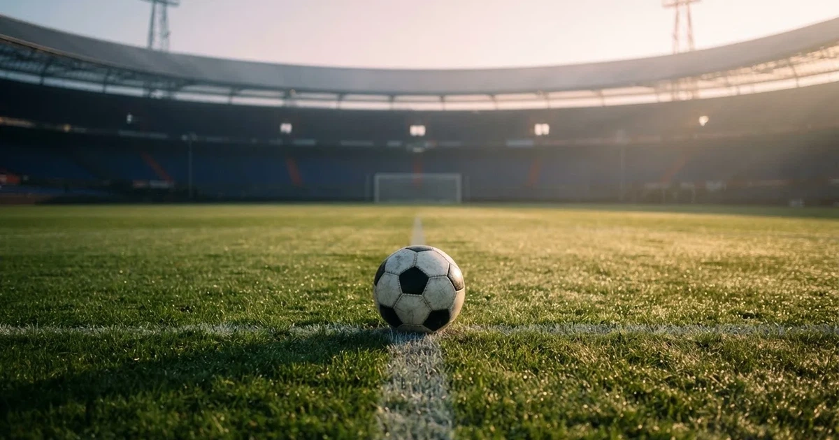 Een voetbal op de middenstip van een grasveld in het ochtendlicht