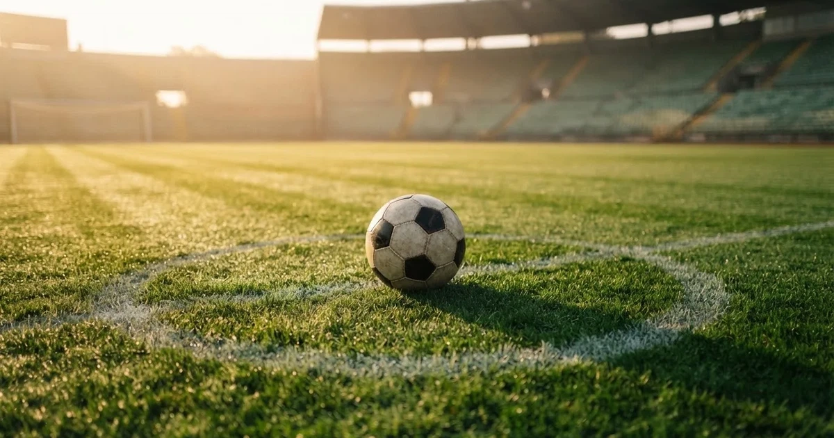 Een voetbal op de middenstip van een grasveld in het ochtendlicht