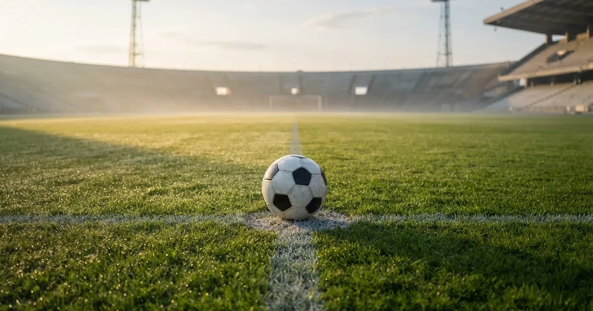 Een voetbal op de middenstip van een grasveld in het ochtendlicht