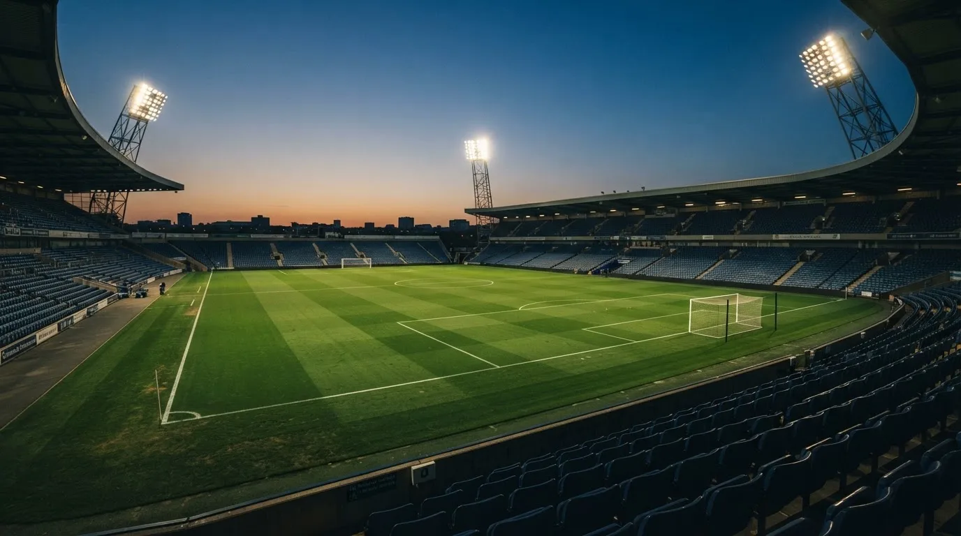 Een leeg voetbalstadion met lichtmasten bij schemering