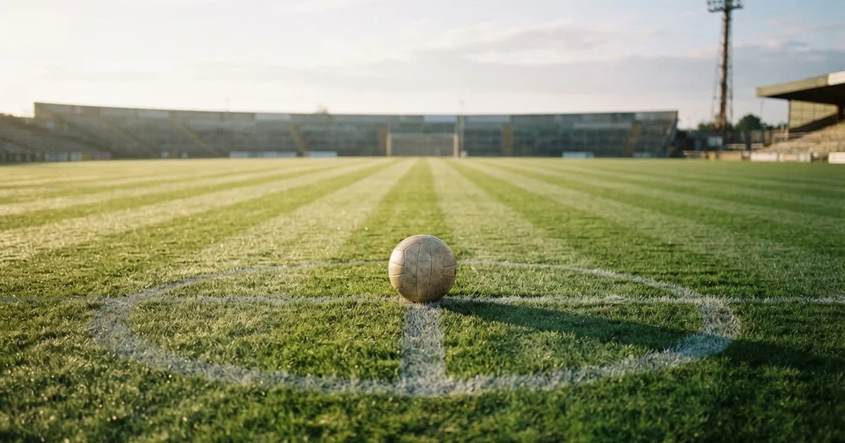 Een voetbal op de middenstip van een grasveld in het ochtendlicht