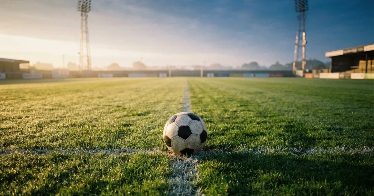 Een voetbal op de middenstip van een grasveld in het ochtendlicht